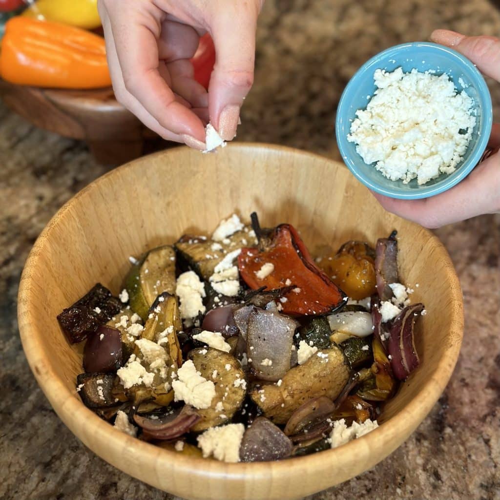 Feta cheese being crumbled on top of roasted vegetables.