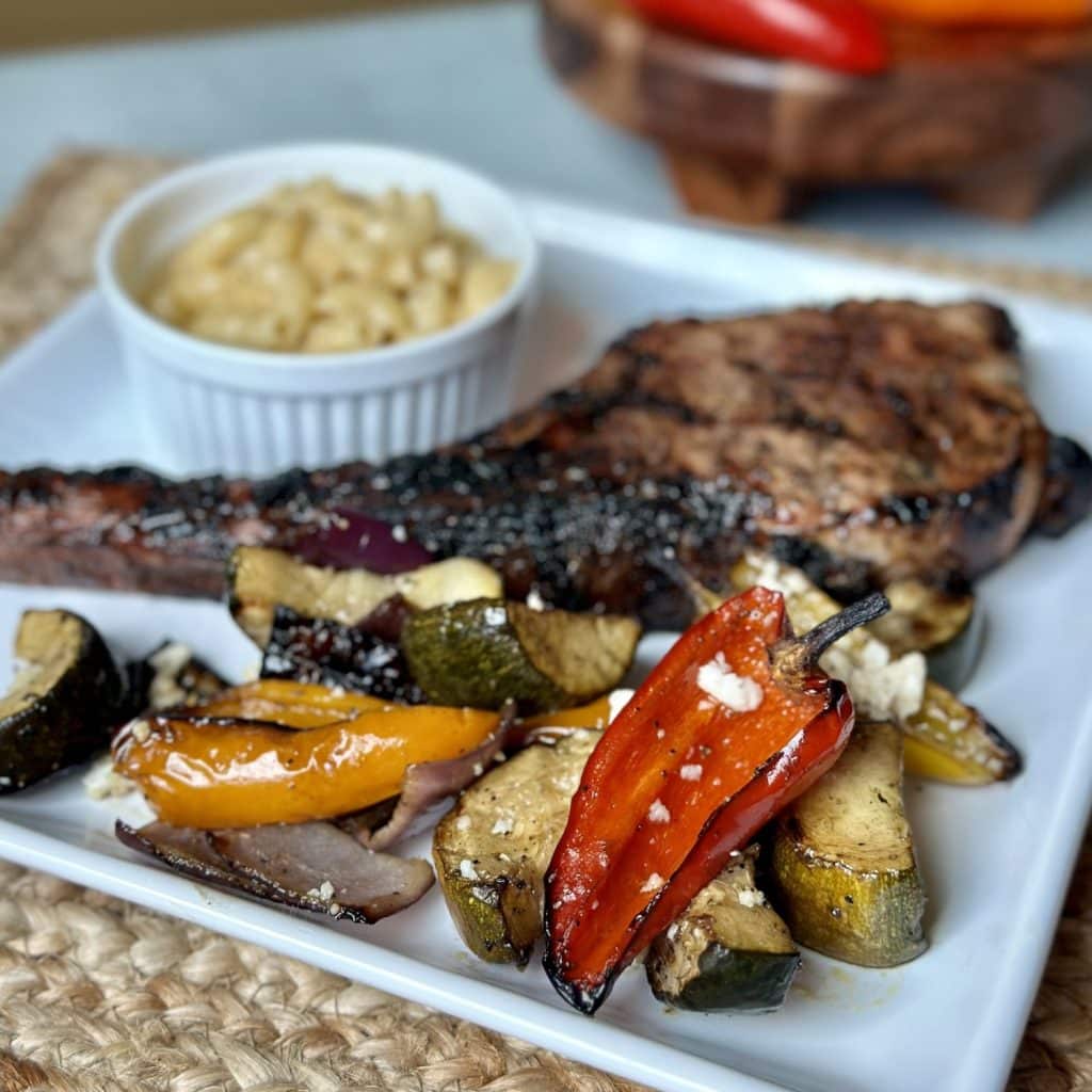 Roasted vegetable salad with a pork chop and mac and cheese on a plate.