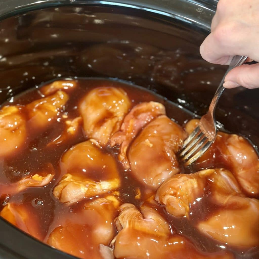Chicken being placed in a honey garlic sauce in a crockpot.
