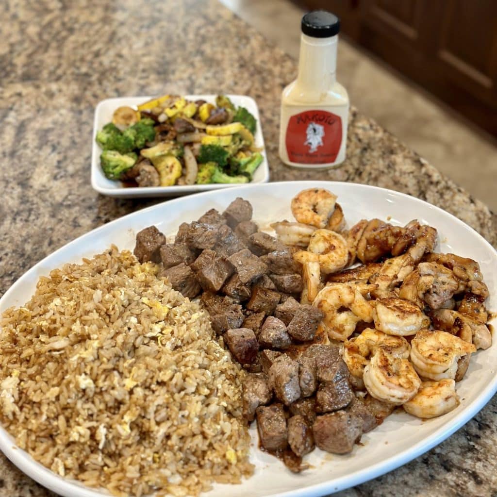 A plate of hibachi chicken, rice, steak and fried rice with a side of vegetables.