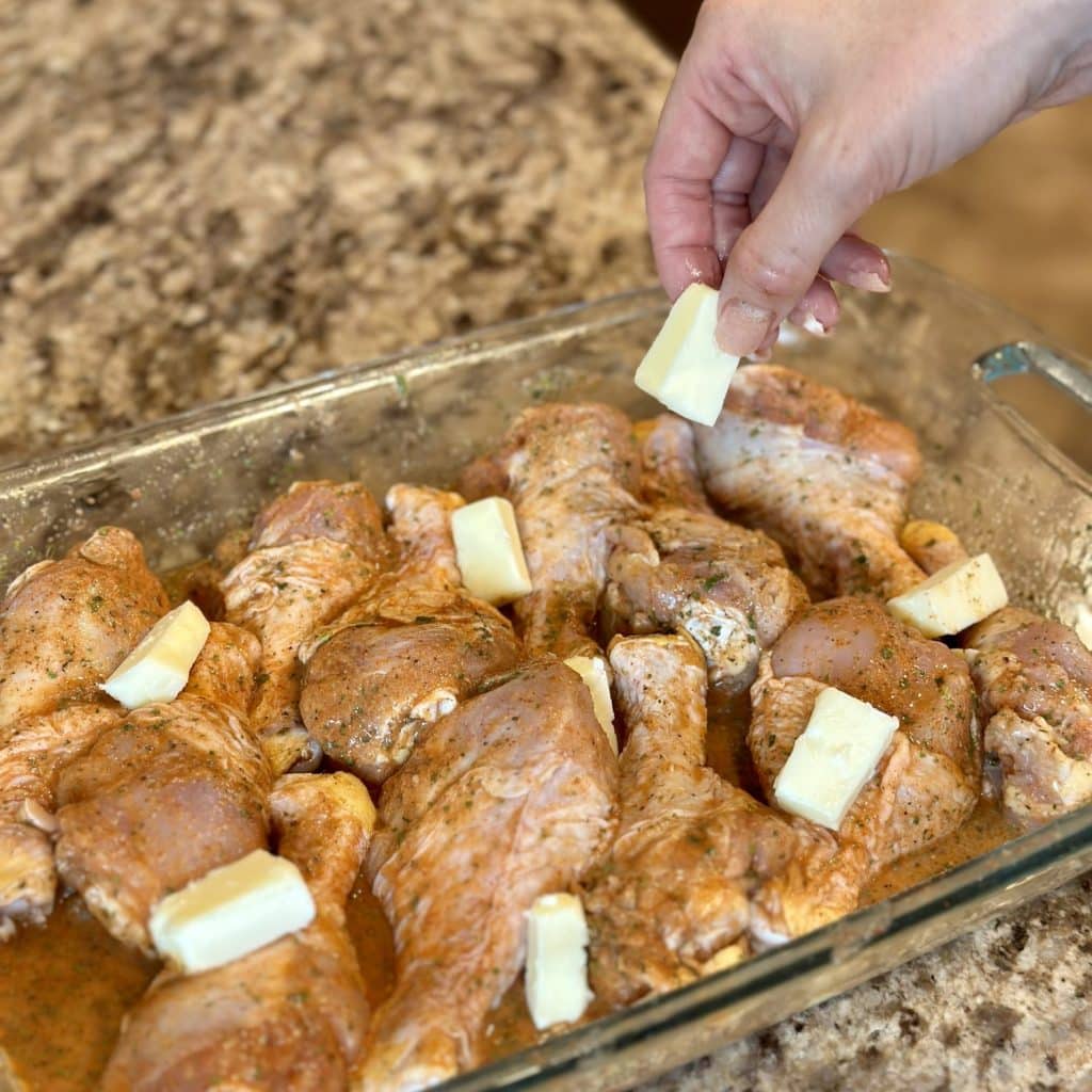 Adding butter on top of drumsticks in a baking dish.