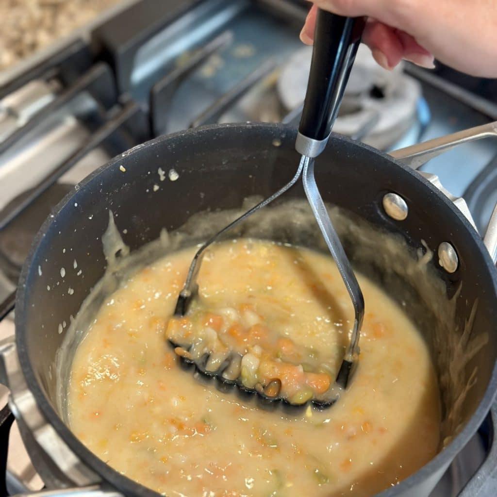 Mashing vegetables in a saucepan of soup.