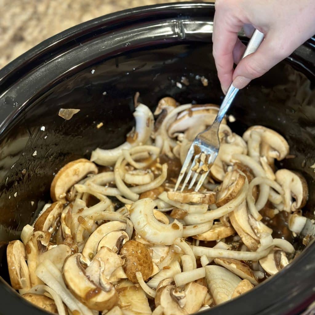 Mixing onions and mushrooms in a crockpot with French onion soup.