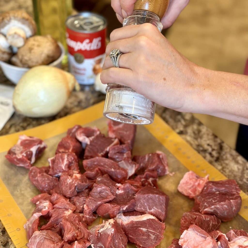 Seasoning a cut up chuck roast with salt.