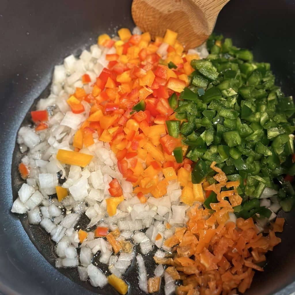 Diced onion and peppers being sautéed in a stockpot.