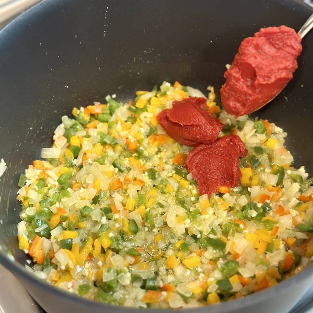 Tomato paste being added to a stockpot of vegetables for chili.