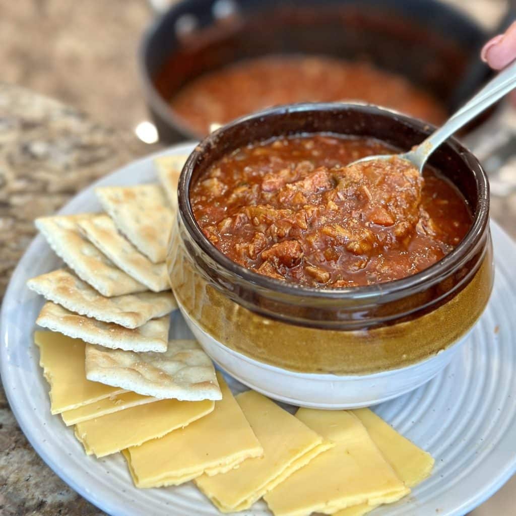 A bowl of brisket chili with cheese and crackers on the side.