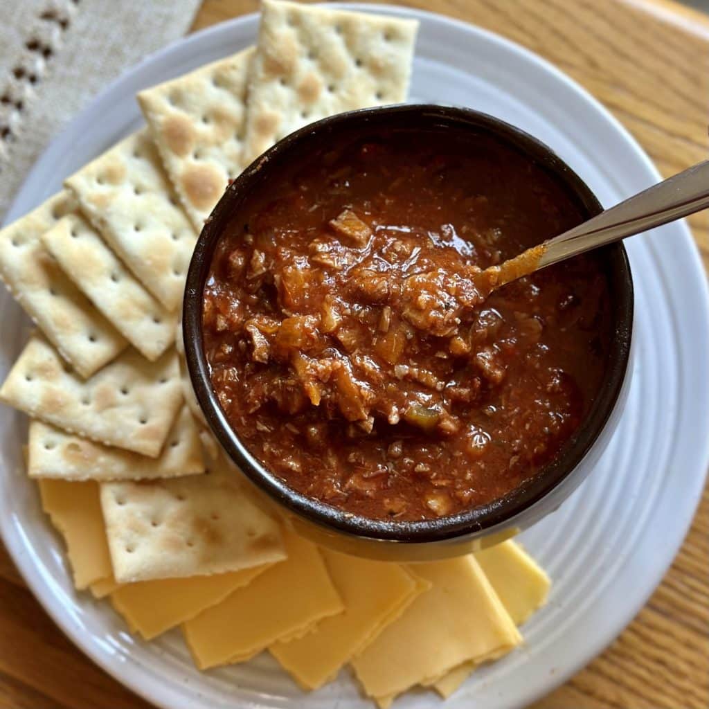 A bowl of brisket chili with cheese and crackers on the side.