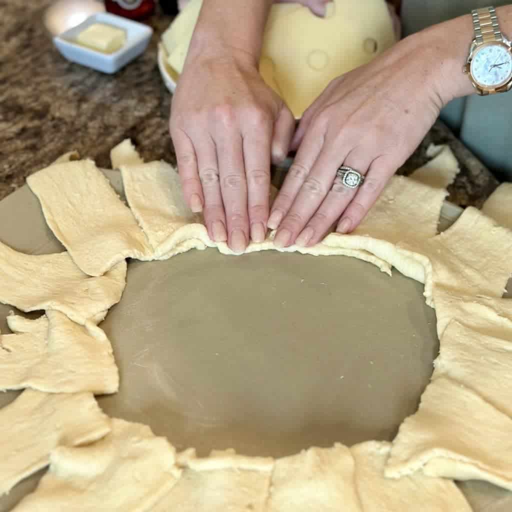 Two hands pressing down on crescent rolls on a pizza stone.