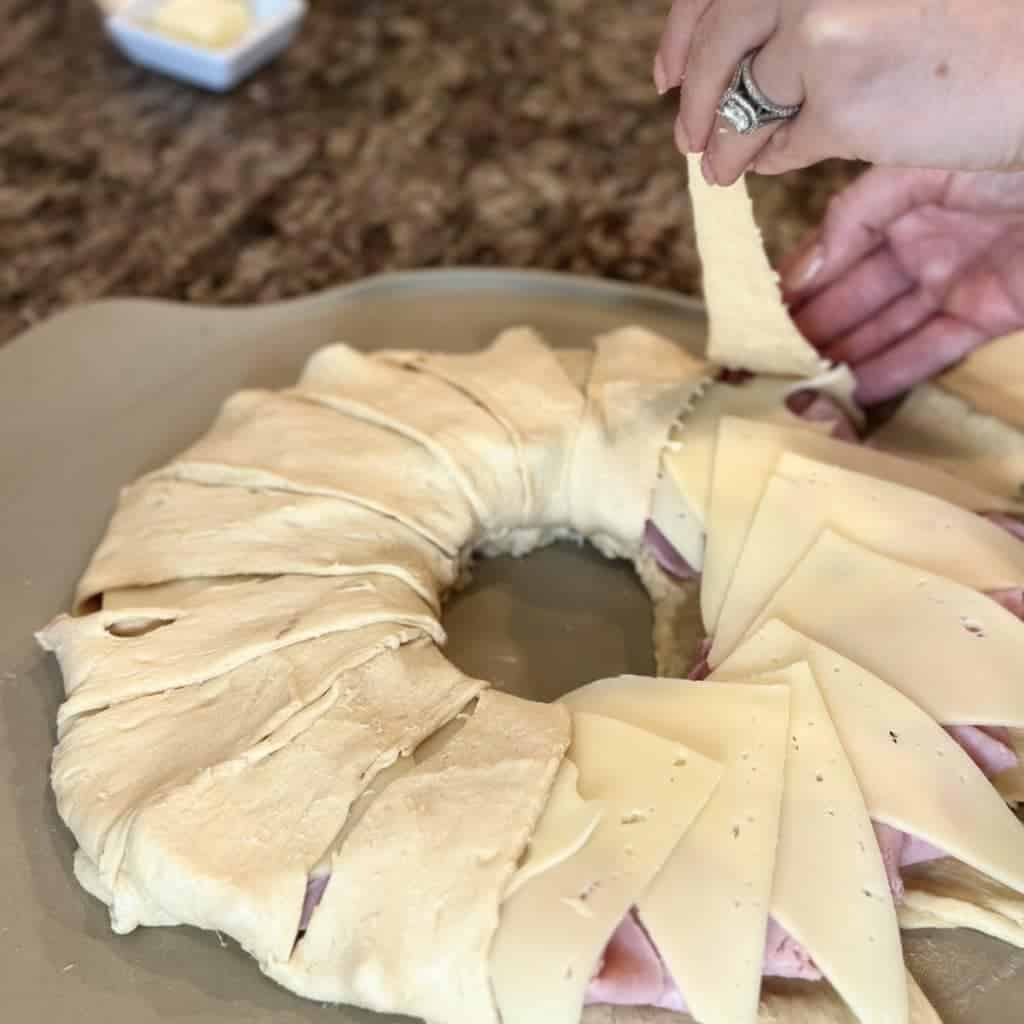 One hand folding crescent roll dough into a circle on a pizza stone.