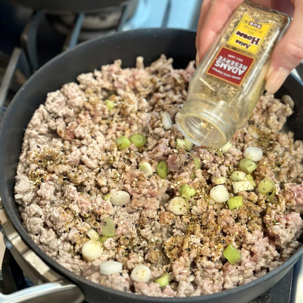 Ground pork being seasoned with Asian seasoning.