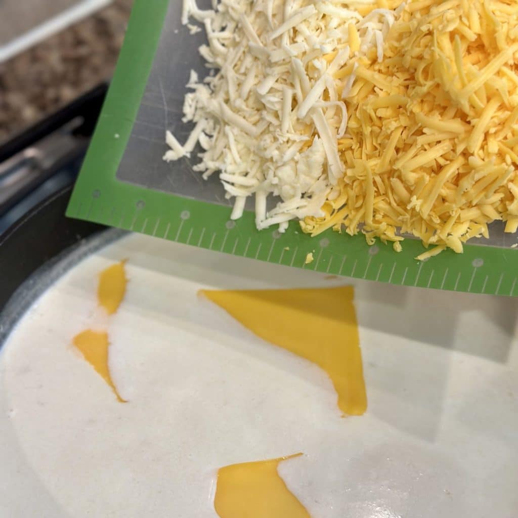 Adding shredded cheese to a cheese sauce.