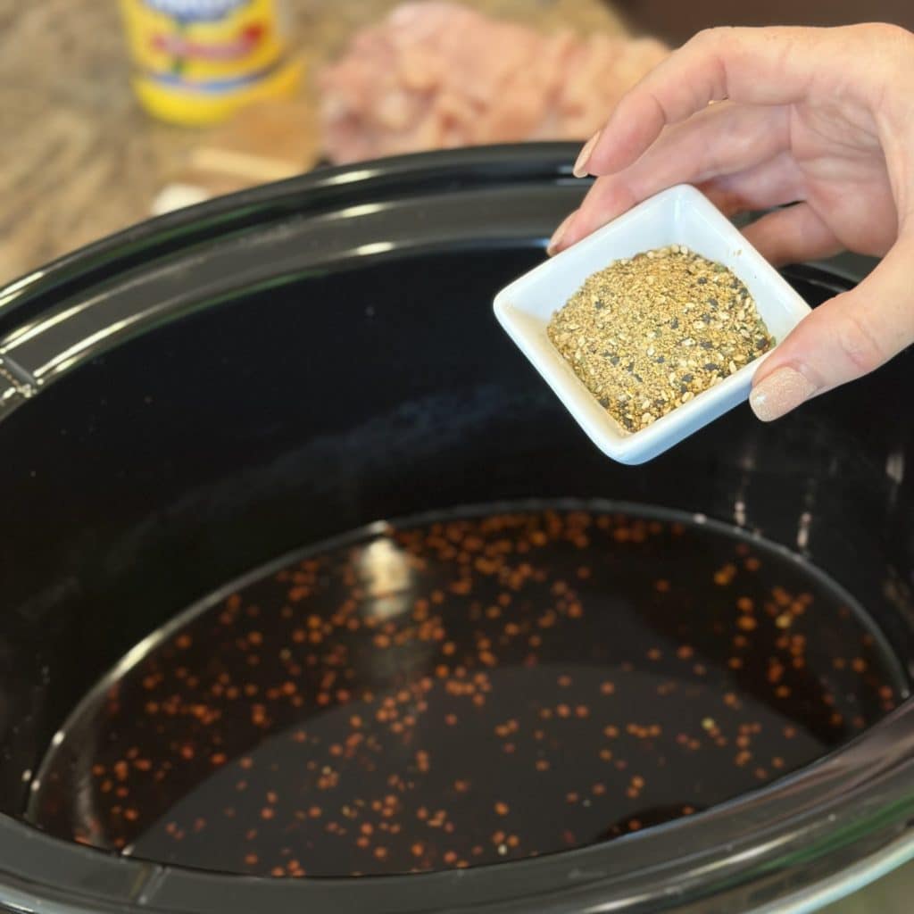 Adding seasoning to a crockpot sauce.