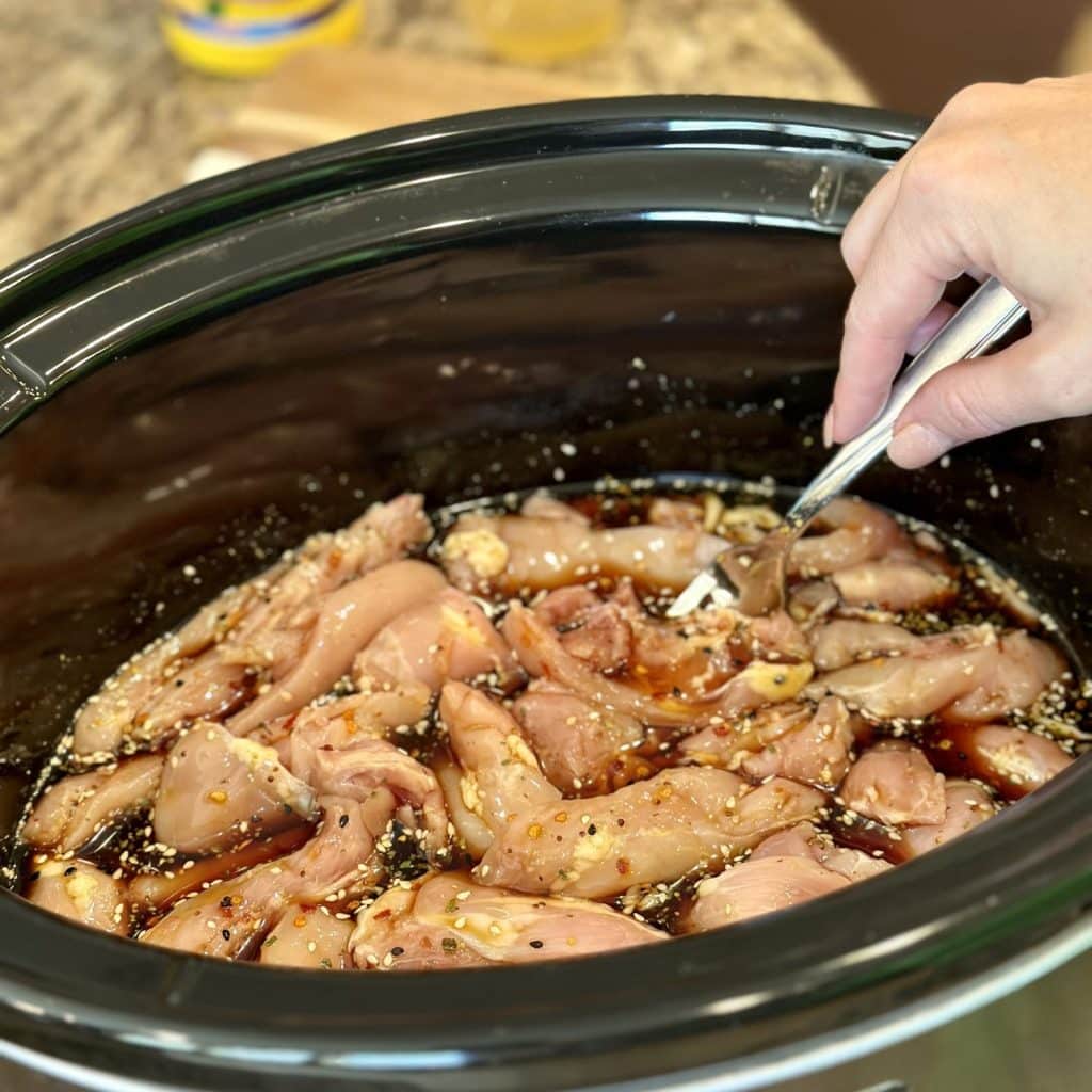 Mixing chicken into a teriyaki sauce in a crockpot.