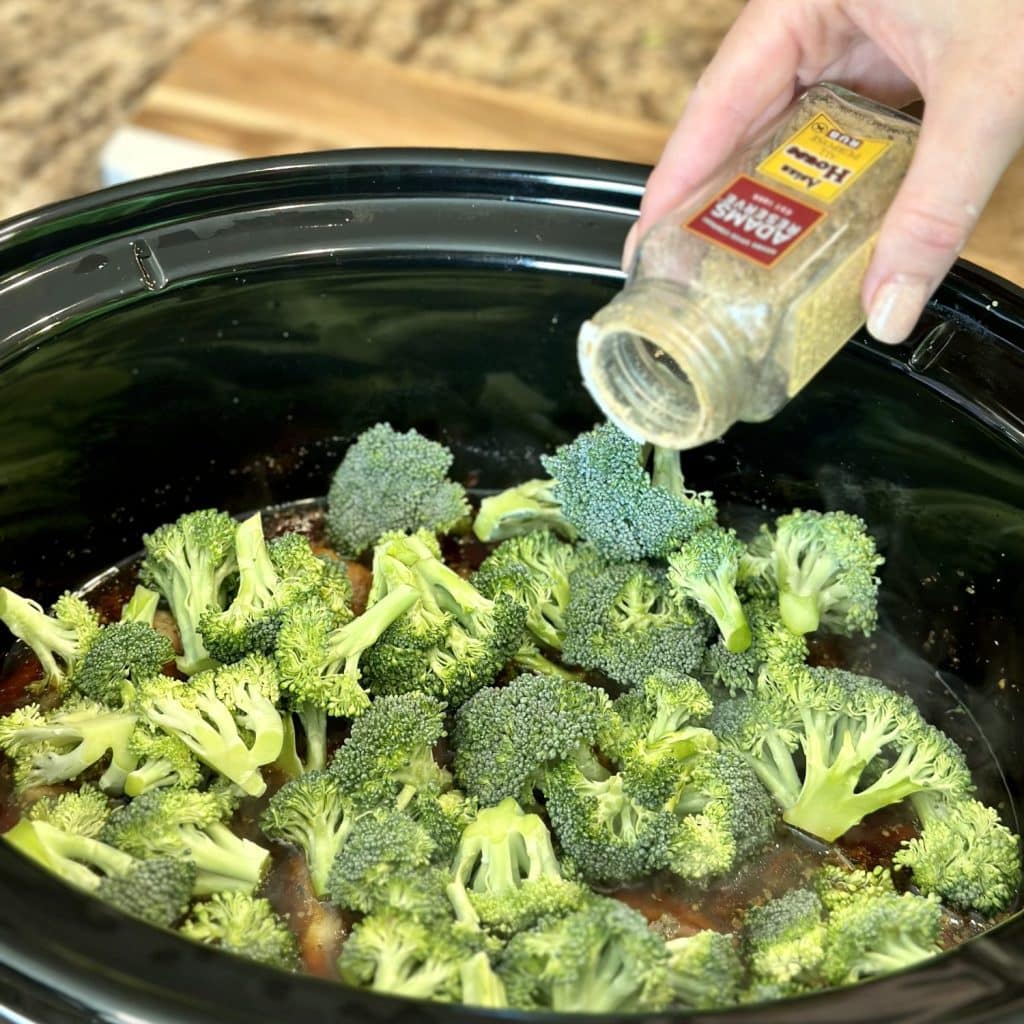 Adding seasoning to broccoli in a crockpot.