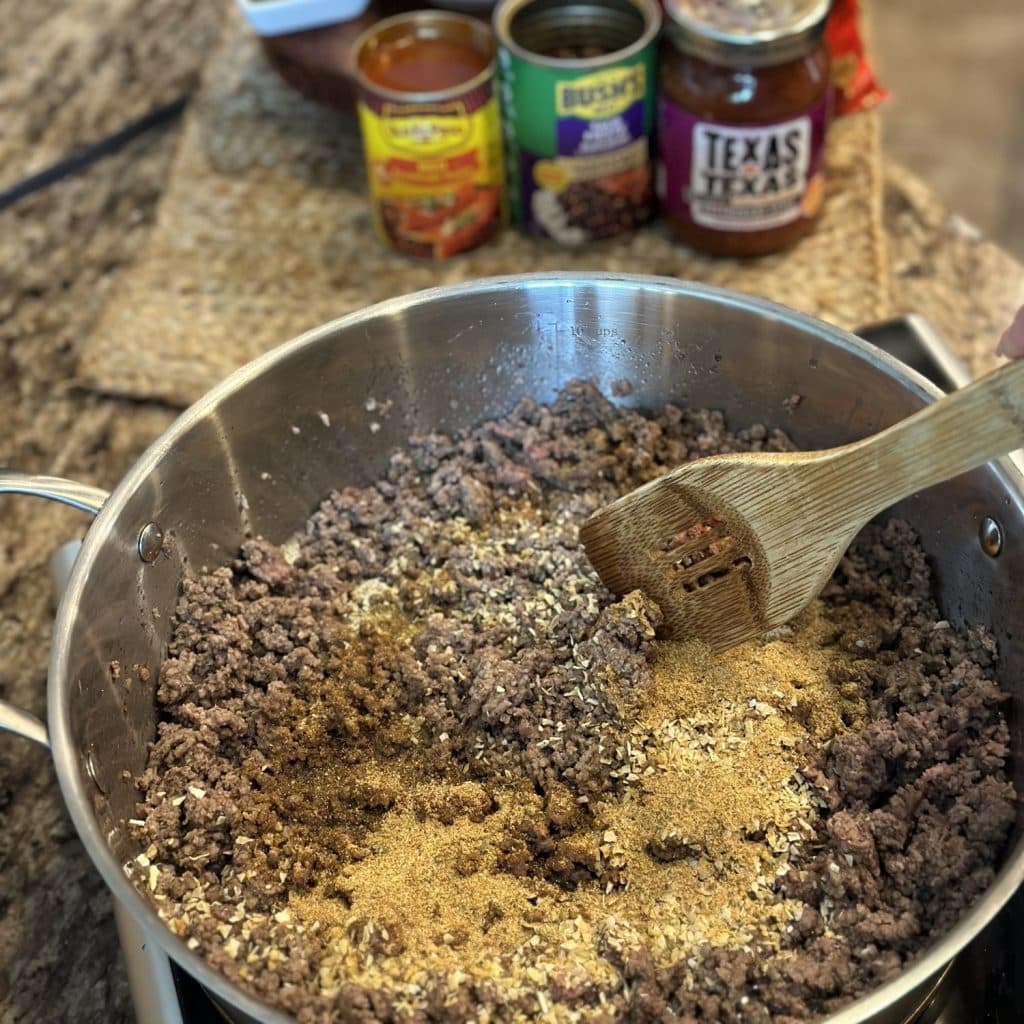 Stirring seasoning into ground beef in a skillet.