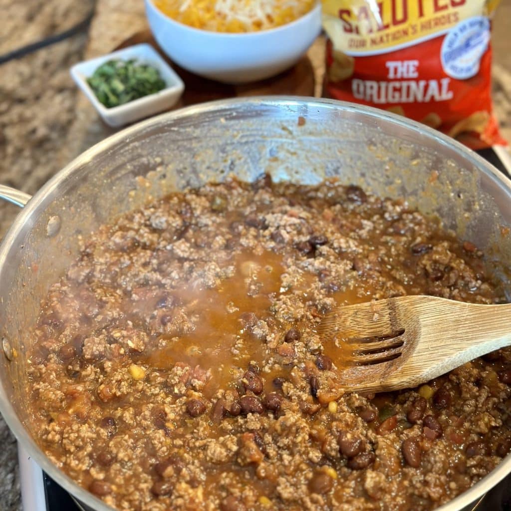 Stirring enchilada sauce, beans, and salsa into ground beef.