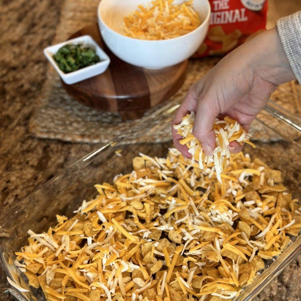 Sprinkling cheese on Fritos in a baking dish.
