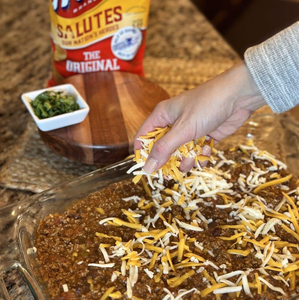 Sprinkling cheese on a ground beef mixture in a baking dish.