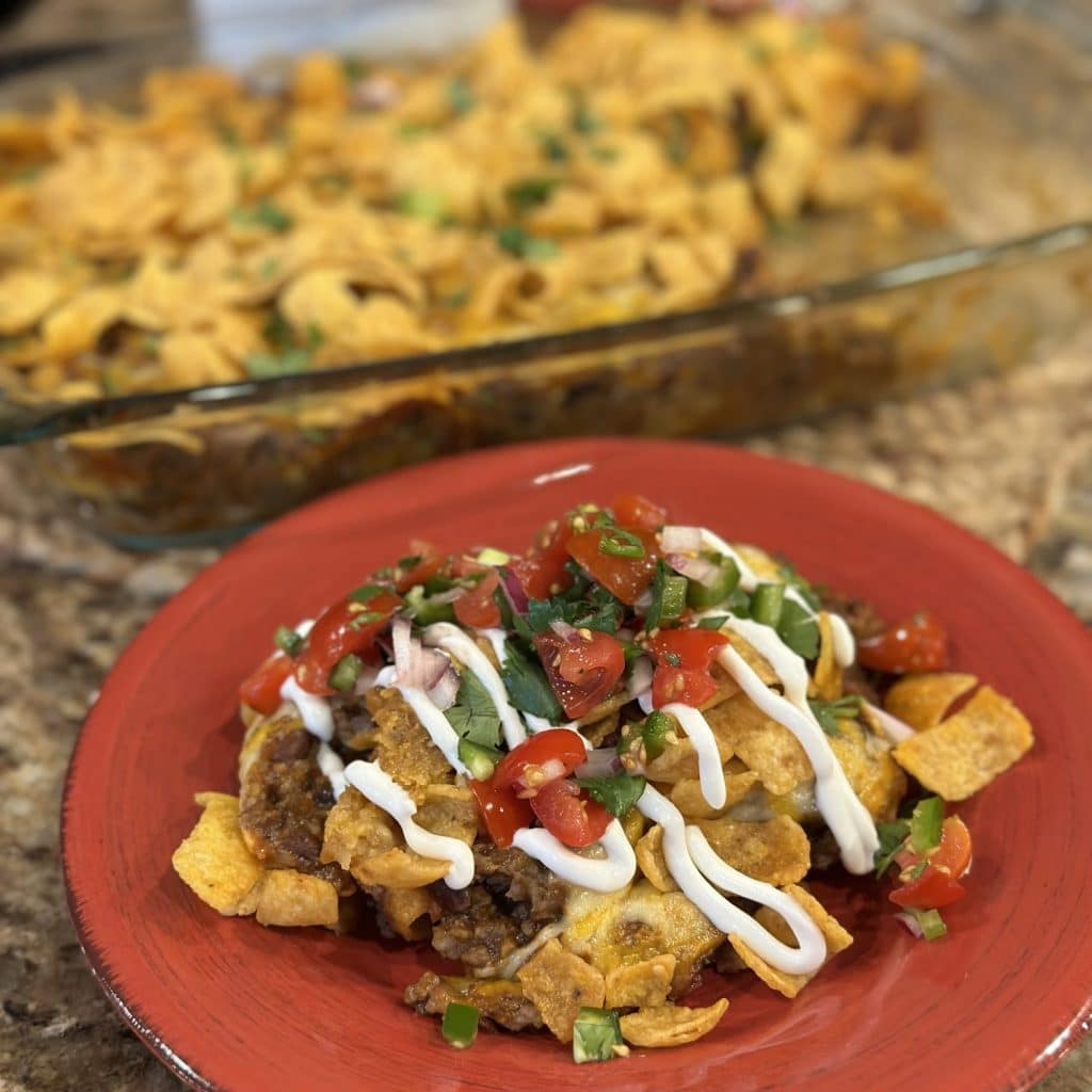 A plate topped with Frito taco pie, sour cream and pico de gallo.