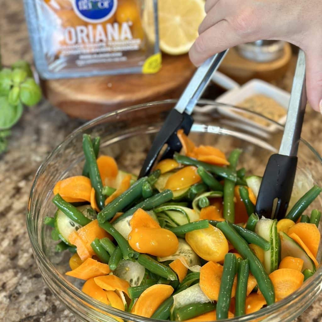 Mixing together vegetables in a glass bowl for a green bean salad.