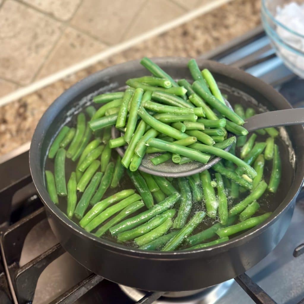 A large skillet with green beans being blanched inside.