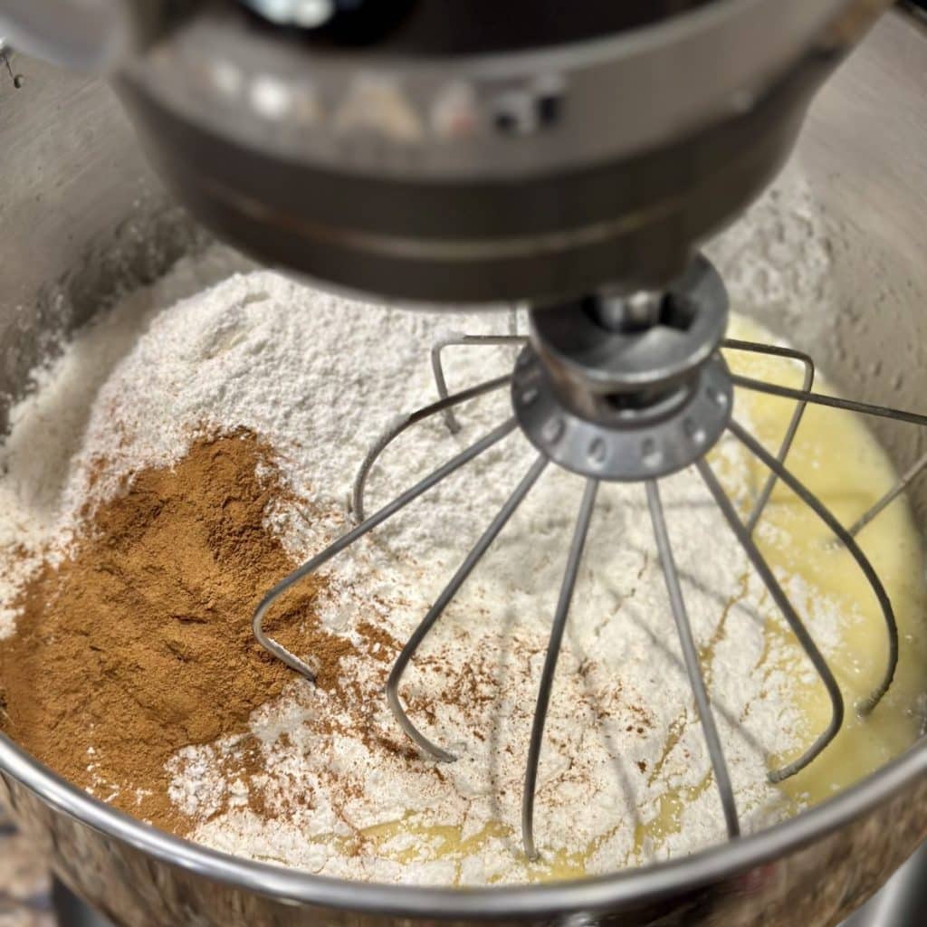 The dry ingredients about to be mixed into wet ingredients for a cake in a mixer.