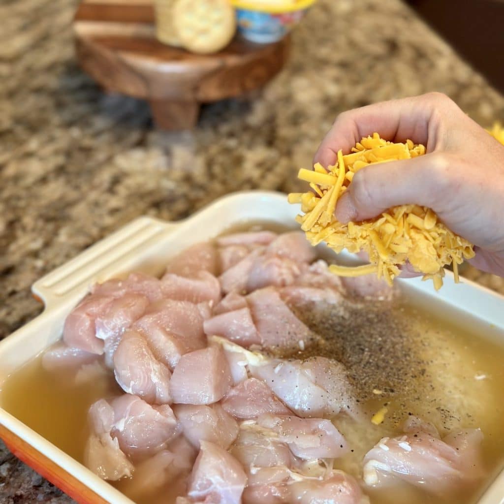 Adding cheese to a baking dish filled with ingredients to make a chicken casserole.