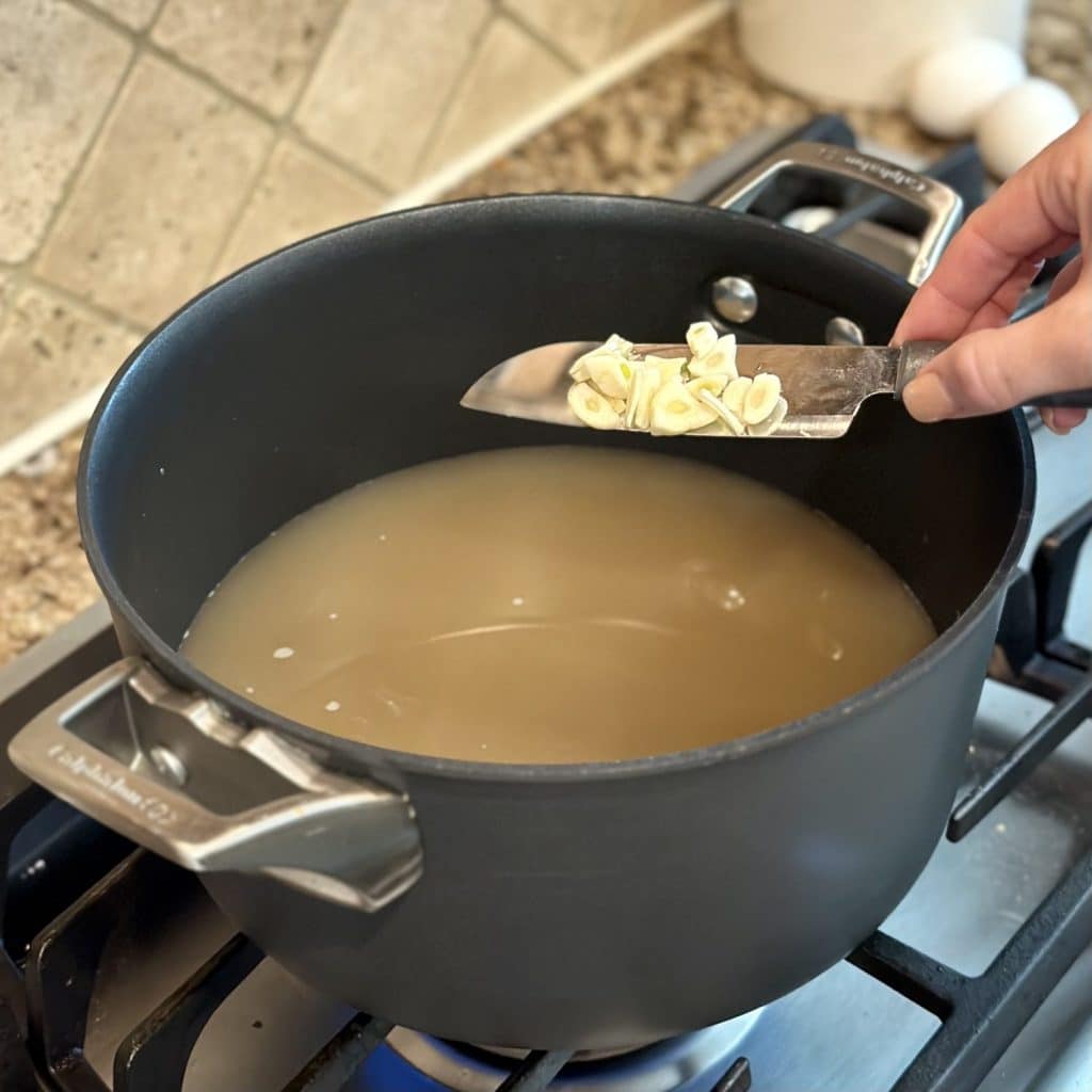 Placing sliced garlic in a pot of broth.