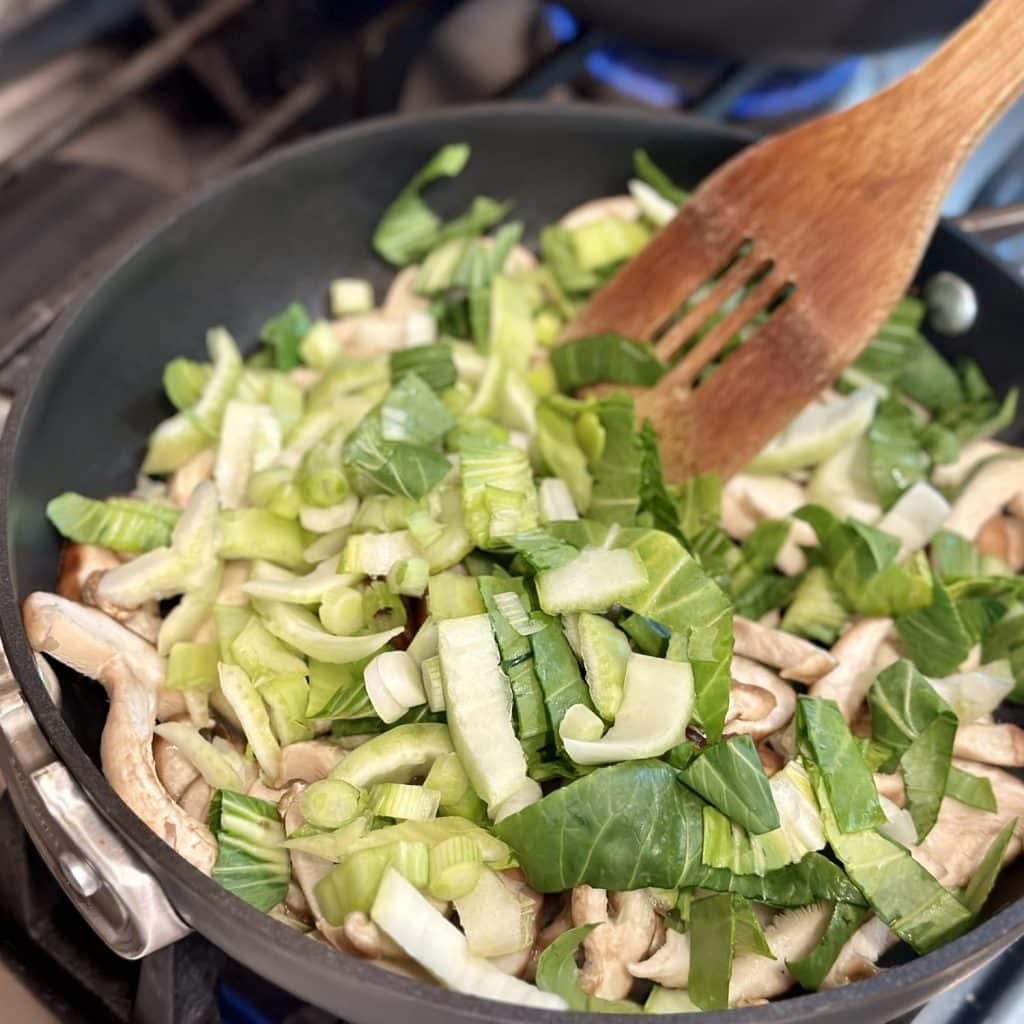 Sautéing mushroom and bok choy in a skillet.