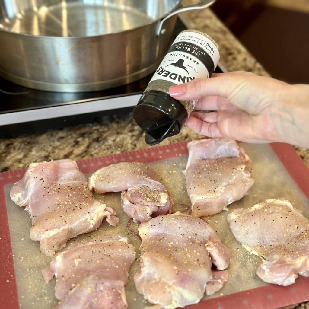 Seasoning chicken thighs on a cutting board.