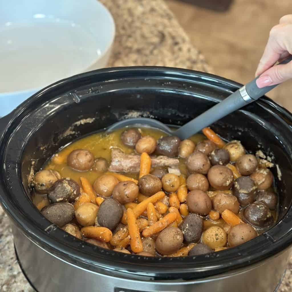 Mixing together cooked vegetables and pork ribs in a crockpot.