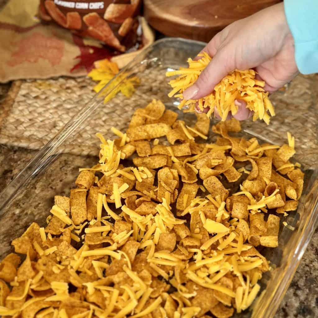 Adding shredded cheese to the top of chips in a baking dish.