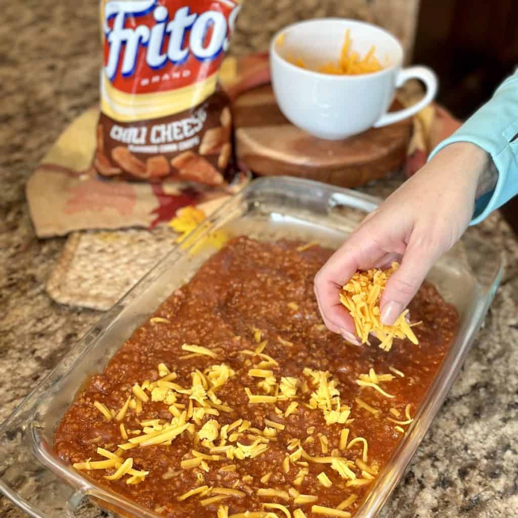 Sprinkling cheese all over the top of chili in a baking dish.