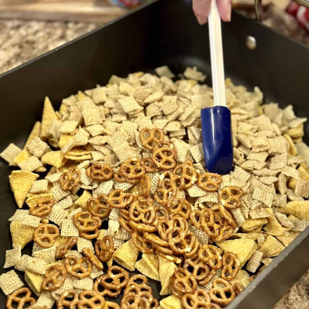 Mixing Chex, bugles and pretzels in a roasting pan.