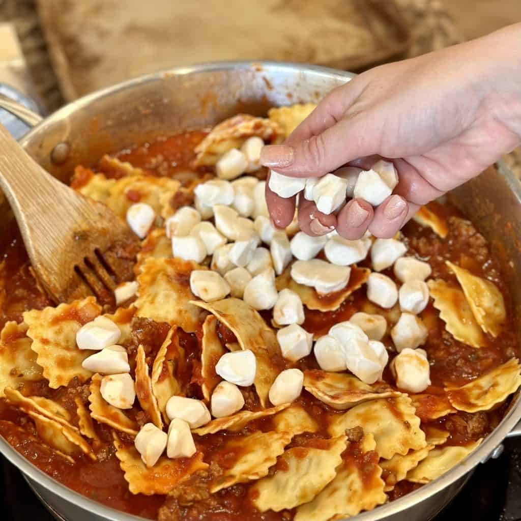 Adding mozzarella pearls to a lasagna filling mixture.