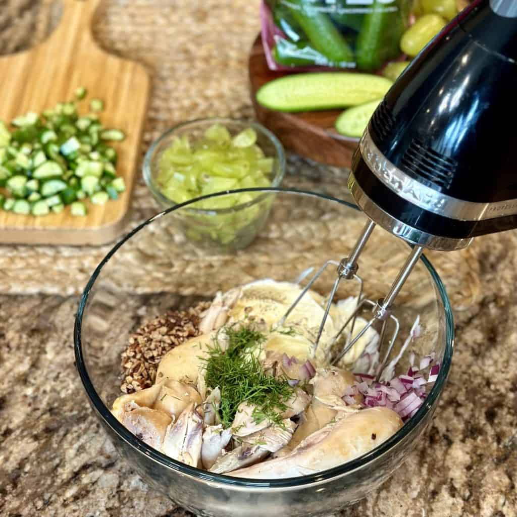 A hand mixer about to blend ingredients in a bowl for chicken salad.