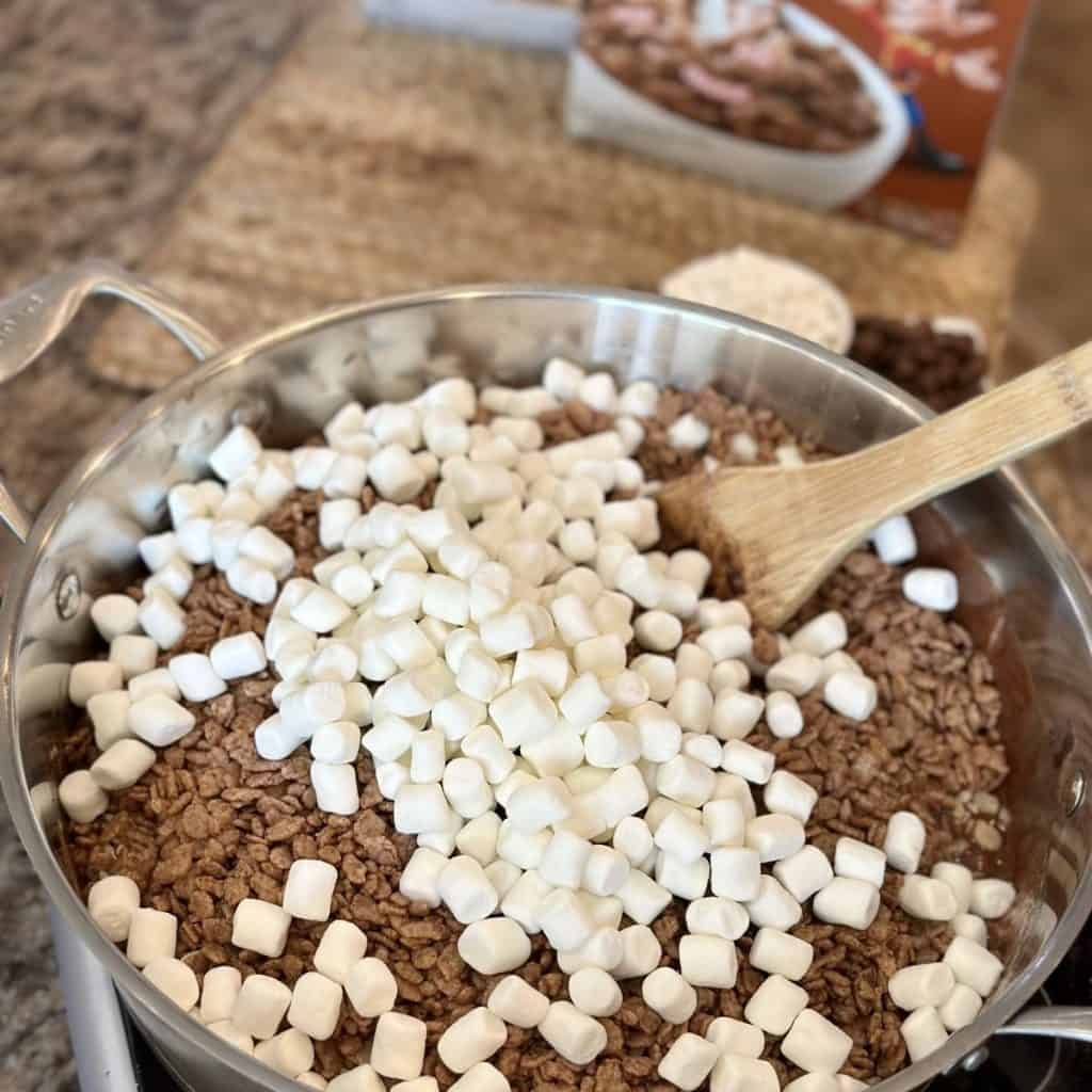 Adding a second load of marshmallows to a skillet for treats.