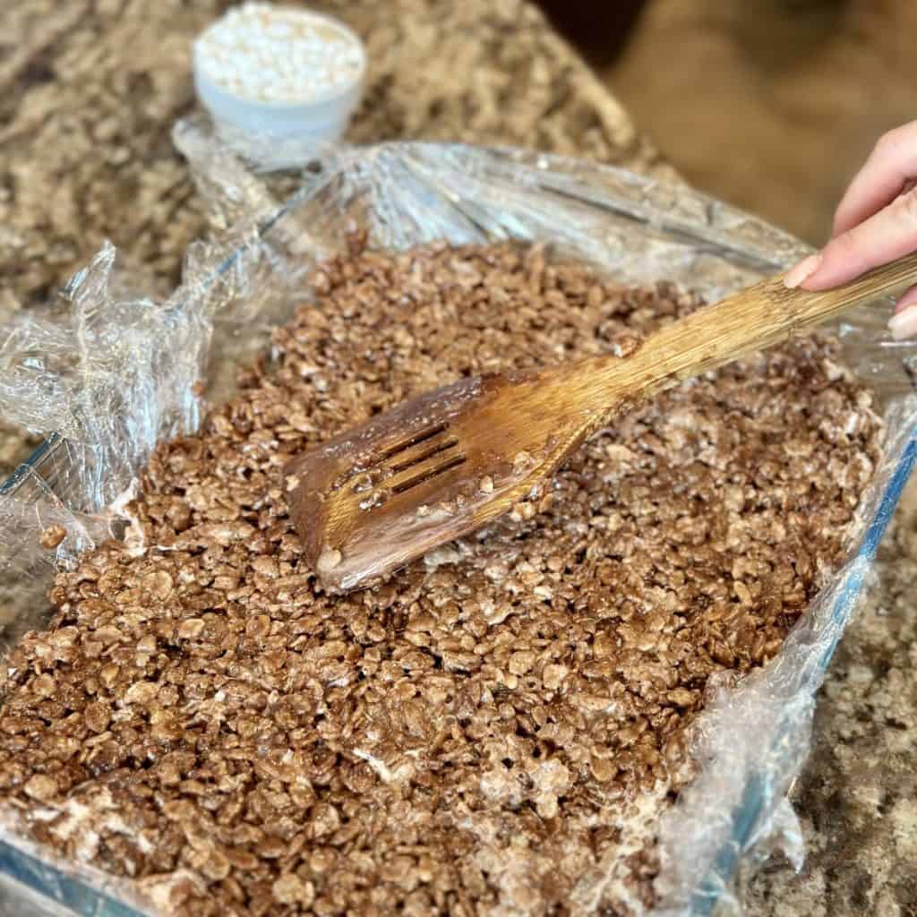 Pressing down chocolate rice Krispy treats in a baking dish.