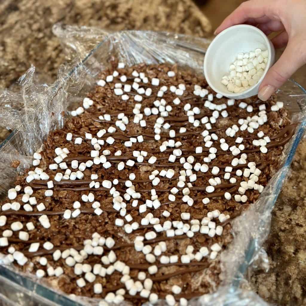 Sprinkling marshmallows in a pan of rice krispy treats.