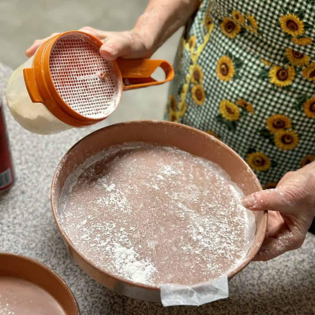 Preparing round pans with flour and parchment paper for a cake.