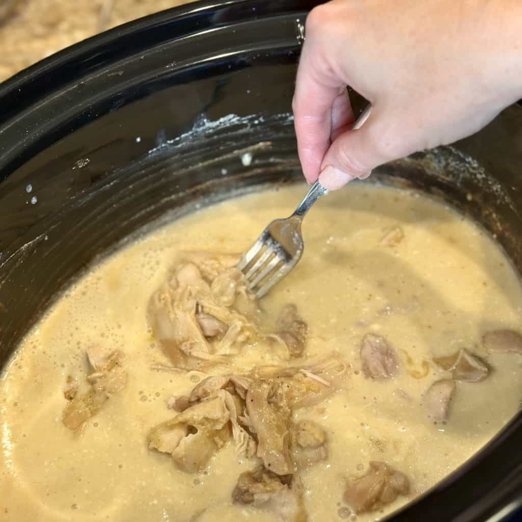 Cutting chicken in a crockpot of gravy.