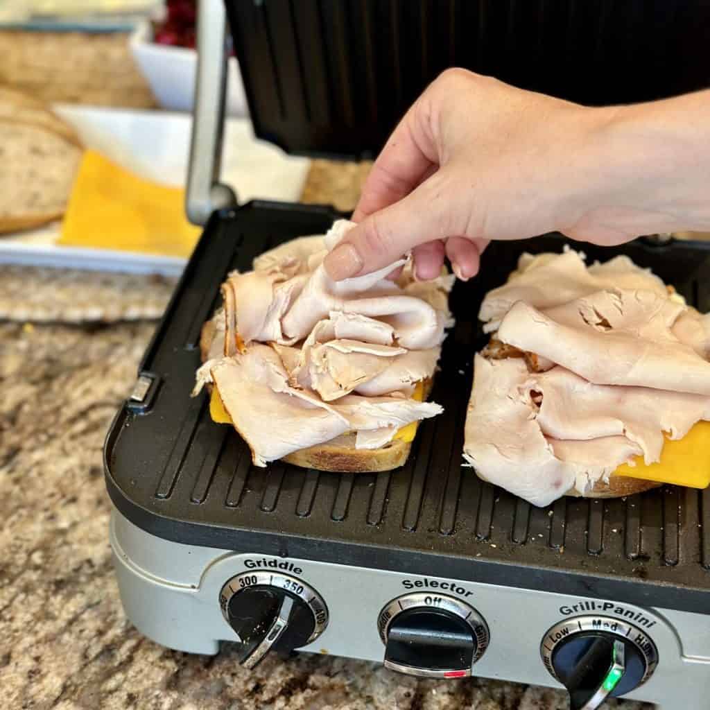Placing turkey on a panini sandwich.