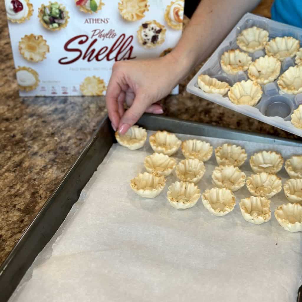 Placing mini phyllo shells on a baking sheet.