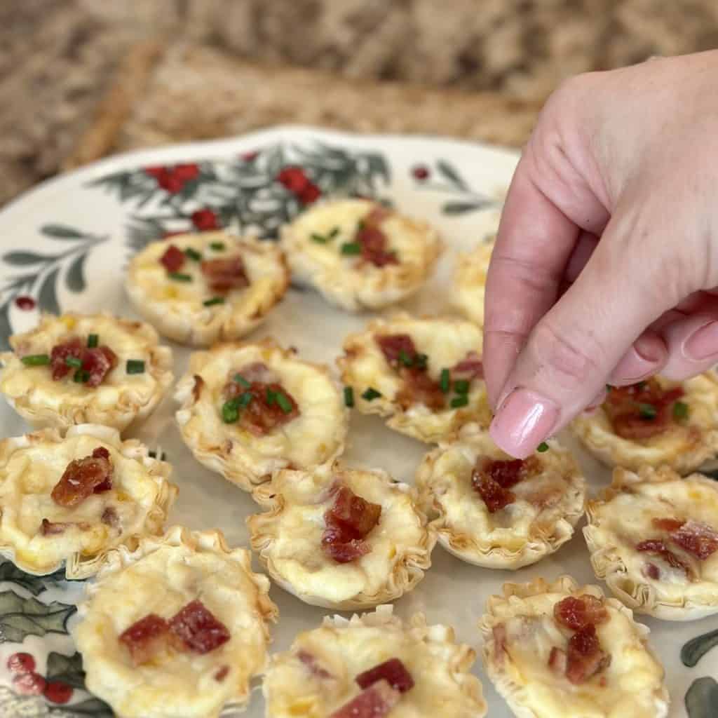 Placing bacon on top of cheese corn tarts.