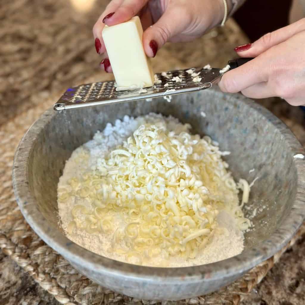 Grating frozen butter in flour in a bowl.