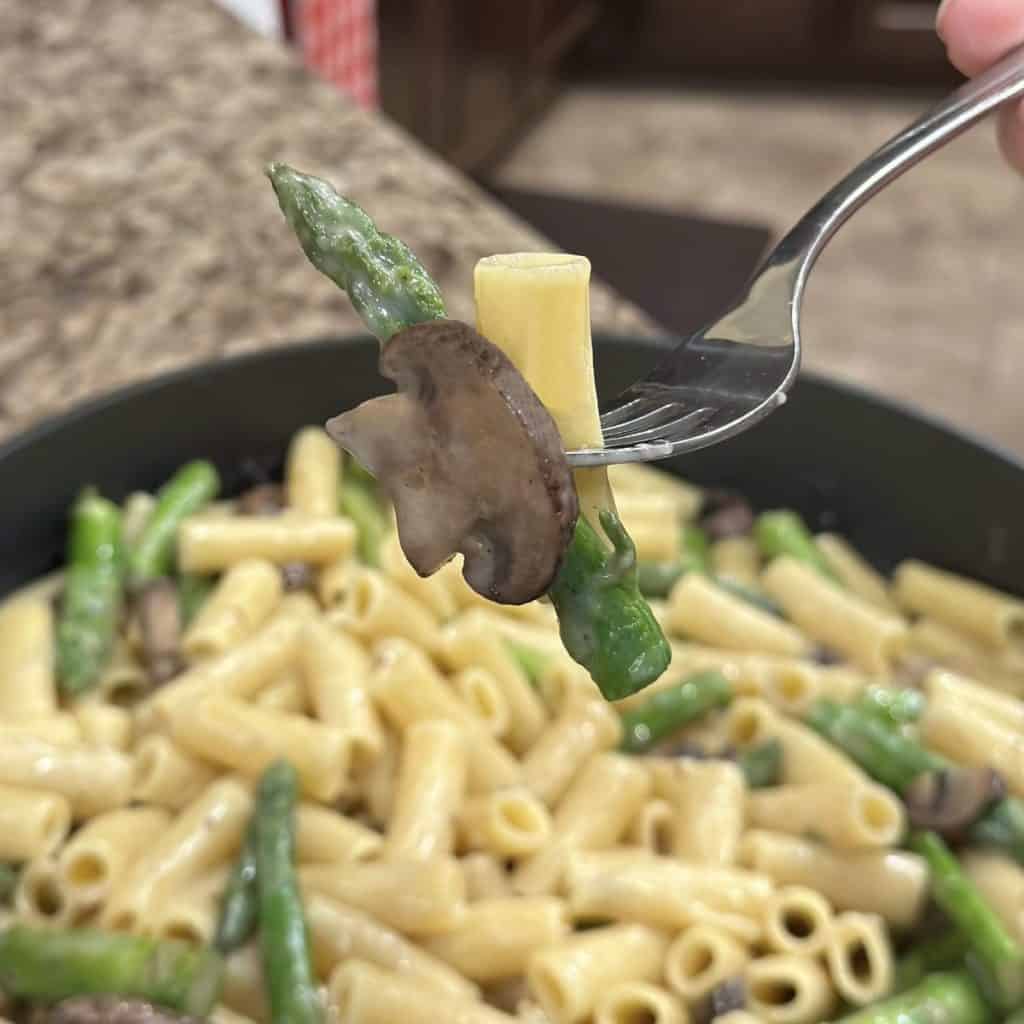 A fork with of pasta and veggies on it.