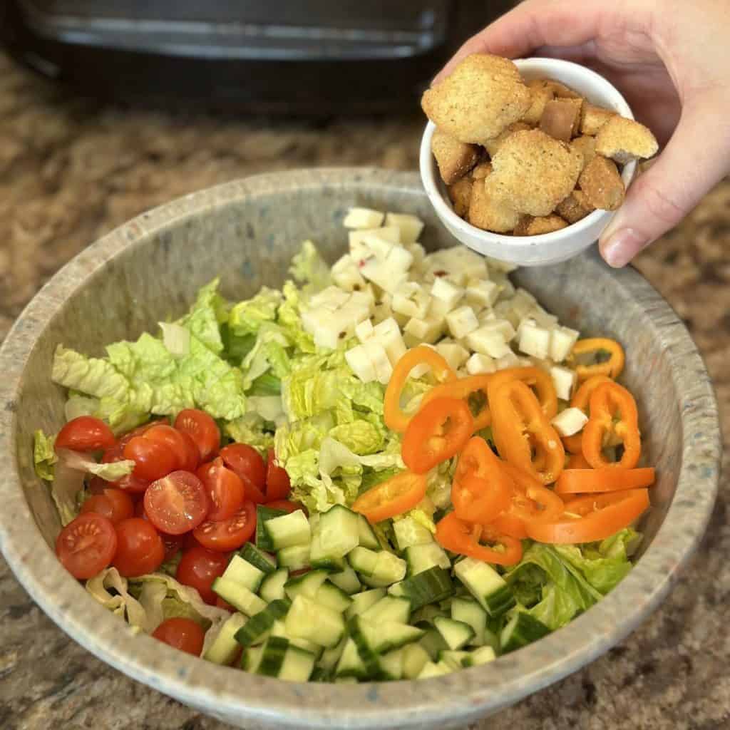 Adding croutons to a bowl of salad ingredients.