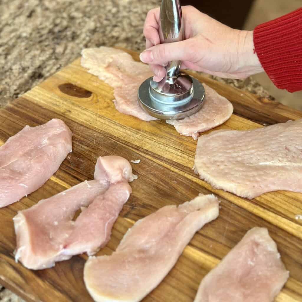 Pounding chicken cutlets on a cutting board.