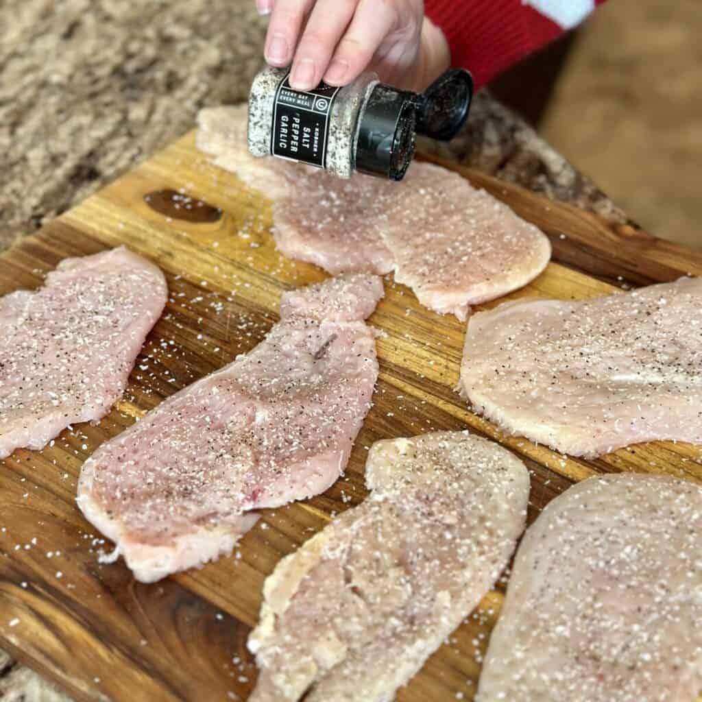 Seasoning chicken cutlets on a cutting board.